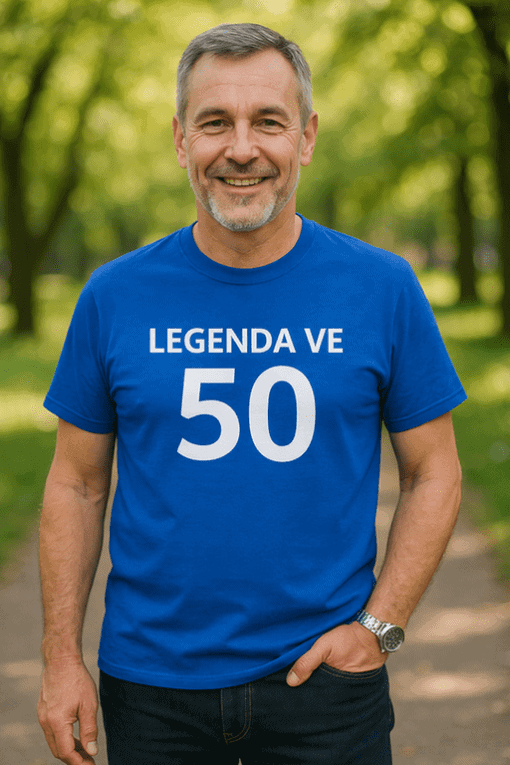 Pohled na šťastného muže v modrém tričku s textem „Legenda ve 50“ v přírodním prostředí.