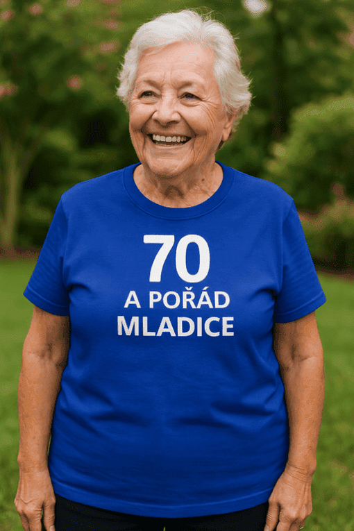 Žena v modrém tričku s nápisem 70 a stále mladá, usmívající se a stojící v přírodě.
