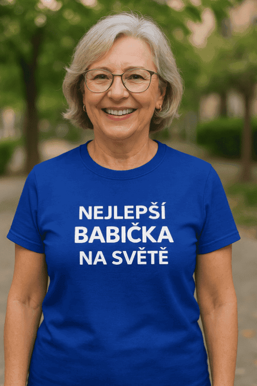 Žena v modrém tričku s nápisem Nejlepší babička na světě, usměvavá, venku v parku.