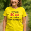 Žena v žluté tričko s nápisem o 50 letech a její úsměv na procházce v přírodě.
