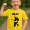 Dítě v žlutém tričku s hasičským motivem, radost a síla, outdoorové prostředí, kluk s výjimečným úsměvem.