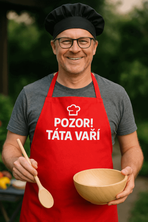 Vizuální popis do popisku alt jpg objekt muž v čepici a zástěře s nápisem POZOR TÁTA VAŘÍ na zahradě, připravující pokrm, radostná atmosféra.