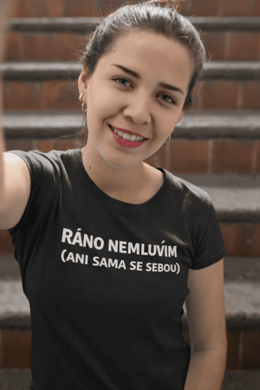 Fotografie mladé ženy na schodech s úsměvem, nosící tričko s vtipným textem.