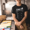 Usměvavý kuchař v kuchyni s kuchařským tričkem Chef, připravený na vaření.