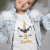 Fotografie dívky v narozeninovém tričku s motivem jednorožce, číslem 3 a jménem Sofie, na ulici.