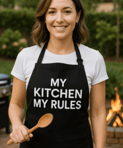 Dáma v triku a zástěře s heslem "My Kitchen My Rules" na zahradě, připravená na vaření.