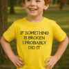 Dítě v žlutém tričku s vtipným nápisem "If something is broken I probably did it" stojí venku v parku.