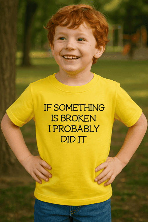Dítě v žlutém tričku s vtipným nápisem "If something is broken I probably did it" stojí venku v parku.