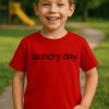 Dítě v červeném tričku s nápisem "laundry day" na trávníku v parku.