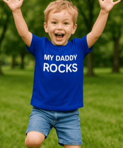 Usmívající se chlapec s tričkem MY DADDY ROCKS, skákající v parku.