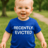 Dítě v modrém tričku s nápisem "Recently Evicted" v přírodním prostředí.